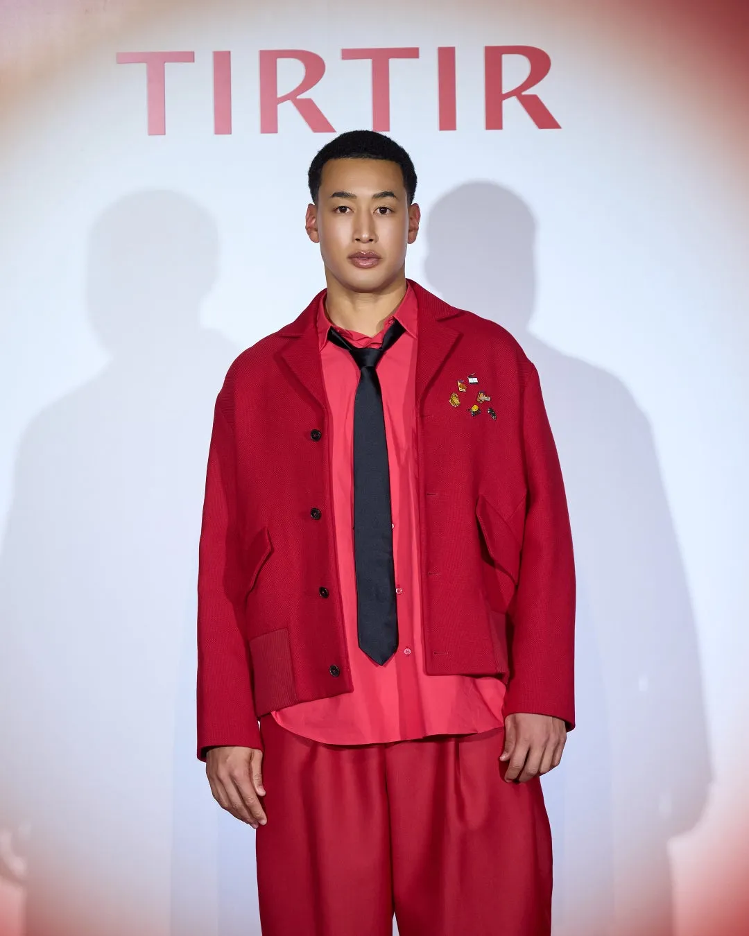 赤い服の男性がTIRTIRロゴの前で