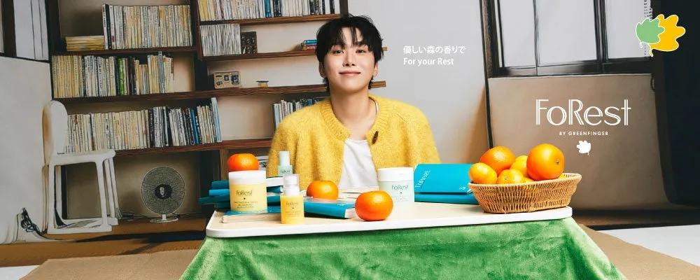 若い男性が、テーブルに置かれた様々な製品と果物、本に囲まれて座っている様子を描いた画像です。背景には本棚があり、リラックスした雰囲気を作り出しています。