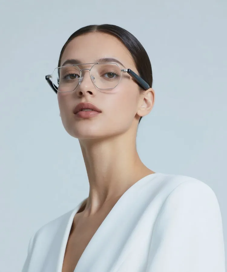 眼鏡をかけた女性のポートレート。女性は白いジャケットを着ており、明るい背景の前に立っています。