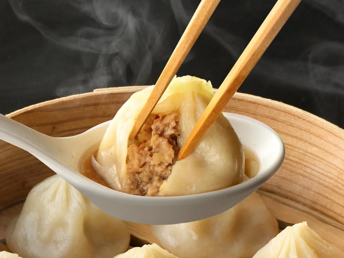 蒸籠に入った小籠包を箸でつまんでいる様子を捉えた写真です。小籠包の中身がよく見え、湯気が立っています。