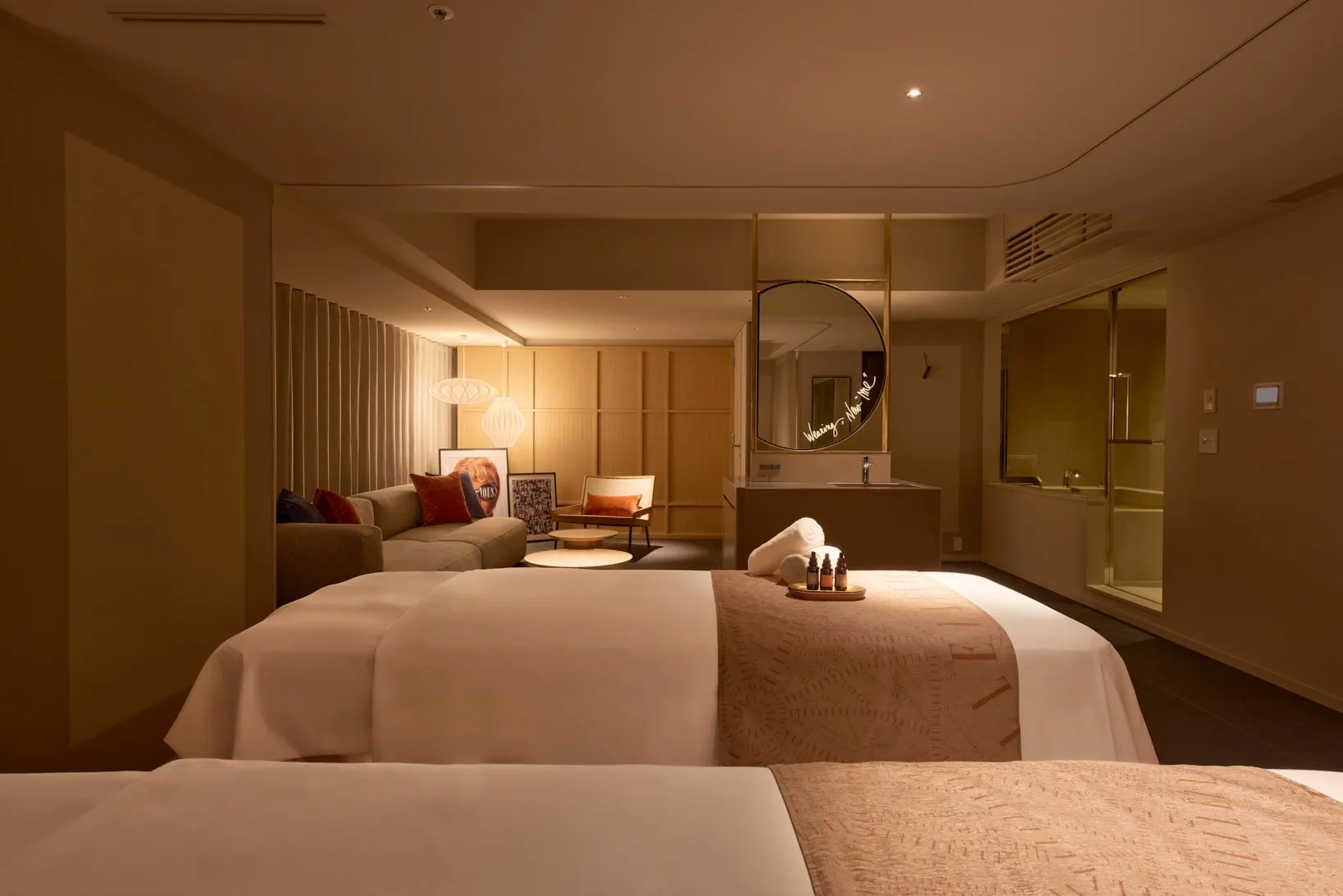 リラックスできるスパルームのインテリア。2台のマッサージベッド、タオル、オイル、鏡、ソファ、椅子が配置されている。