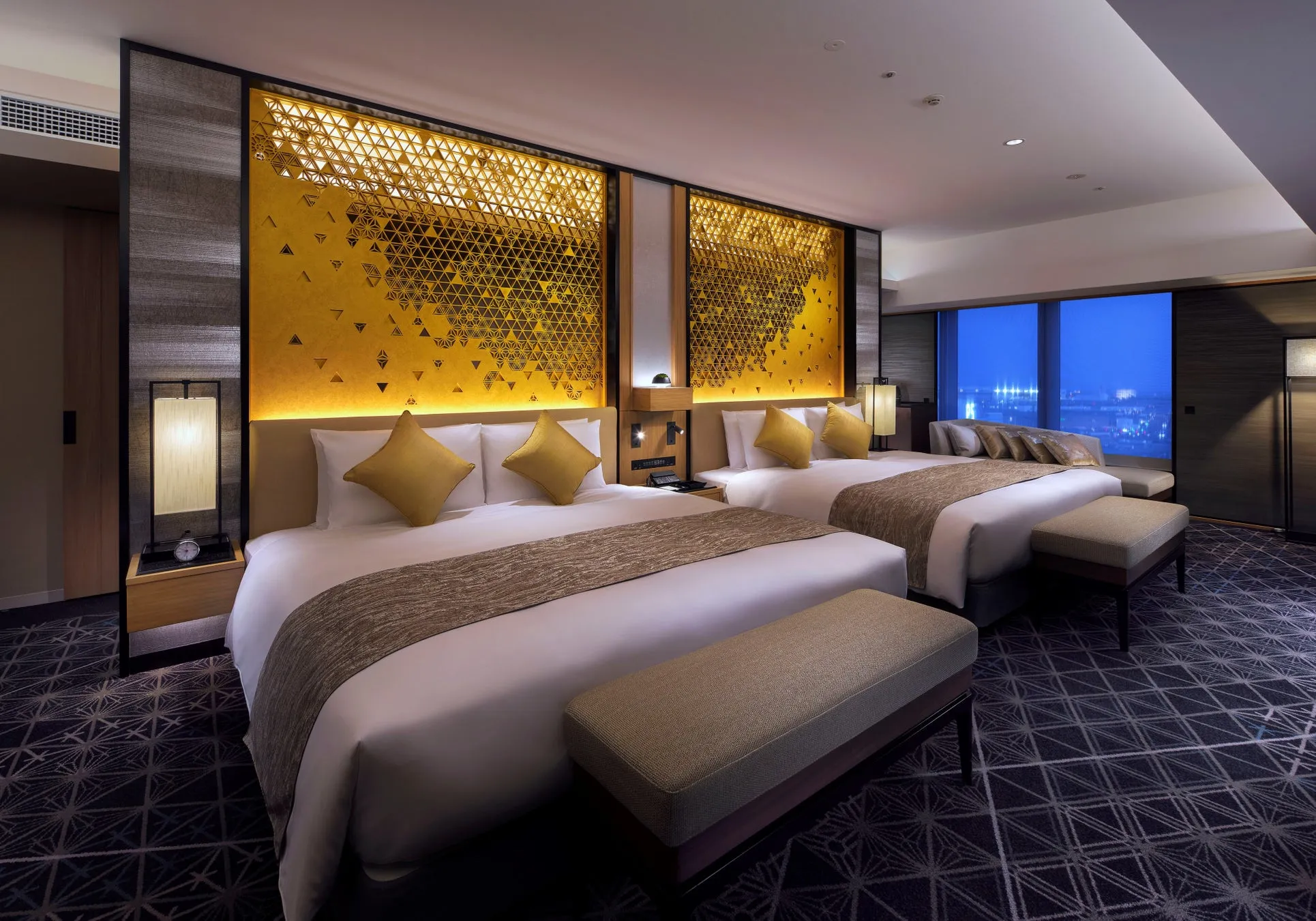 2つのベッドと窓から夜景が見えるホテルの部屋の写真です。