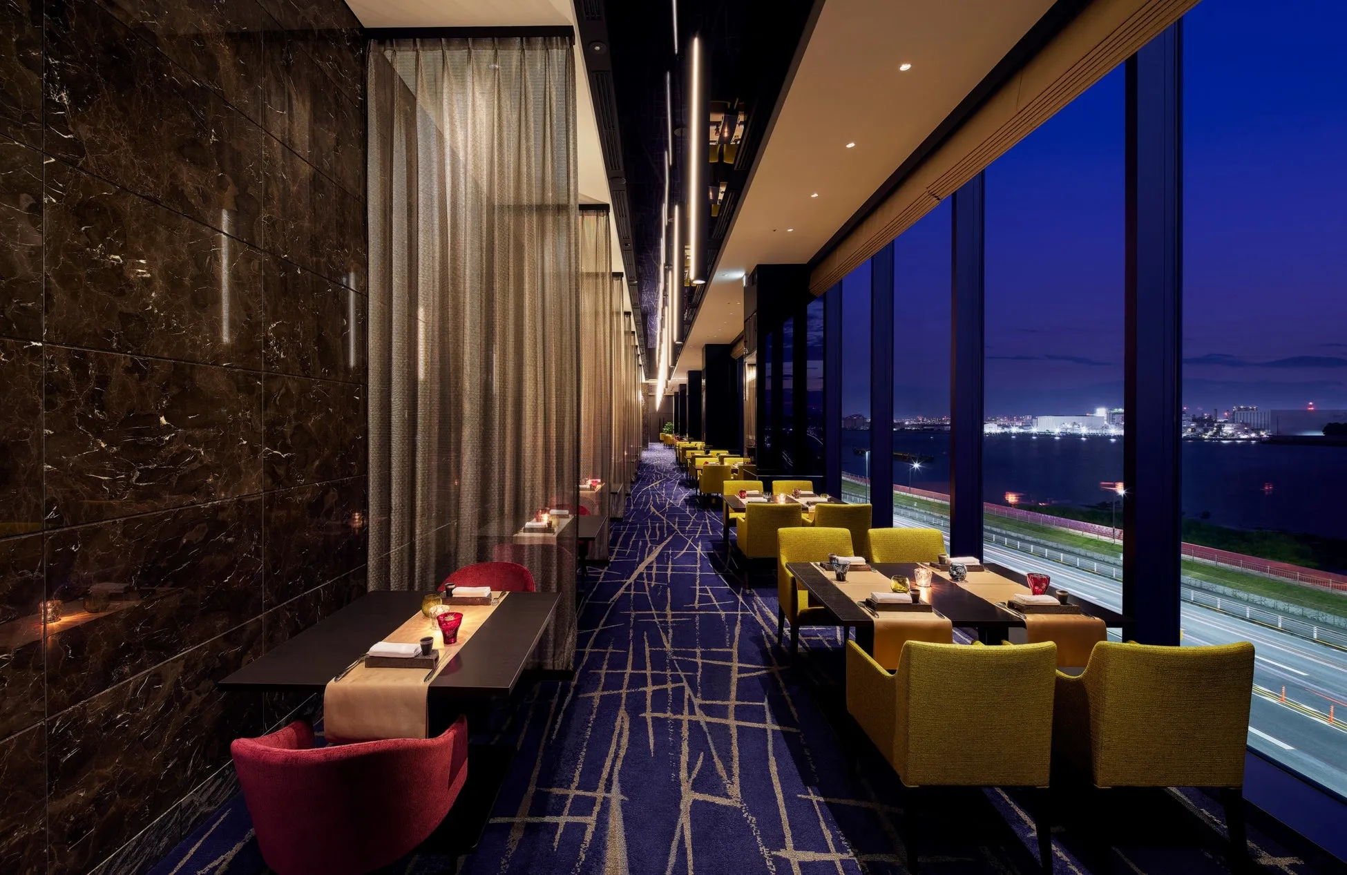 夜のレストランのインテリア。窓から見える夜景と、テーブルと椅子が並んでいる。