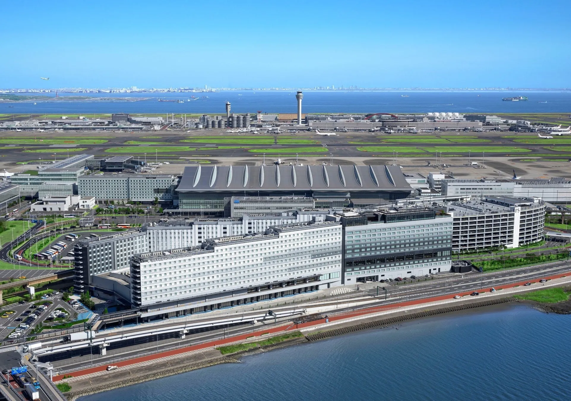 羽田空港の航空写真。空港ターミナル、滑走路、管制塔、ホテル、そして海が見えます。