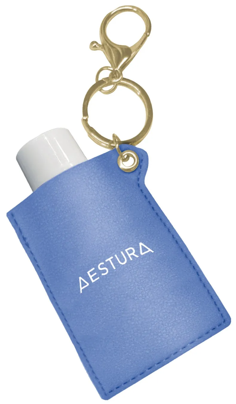 青いケースに入った白いチューブとキーホルダーのクローズアップ写真。ケースには「AESTURA」という文字が書かれています。キーホルダーは金属製で、ケースの上部に接続されています。