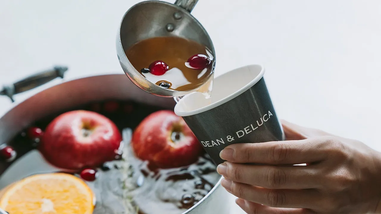 DEAN & DELUCAのカップに飲み物を注いでいる様子。鍋にはリンゴやオレンジ、クランベリーが入っている。