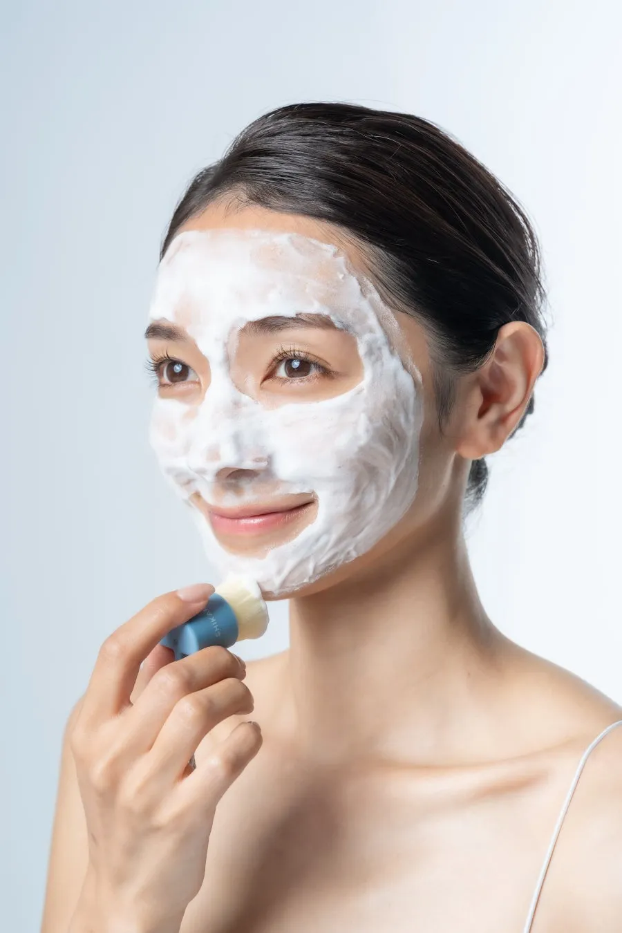 泡洗顔パックをしている女性のポートレート。女性は顔に泡パックをしており、ブラシで洗顔している様子。