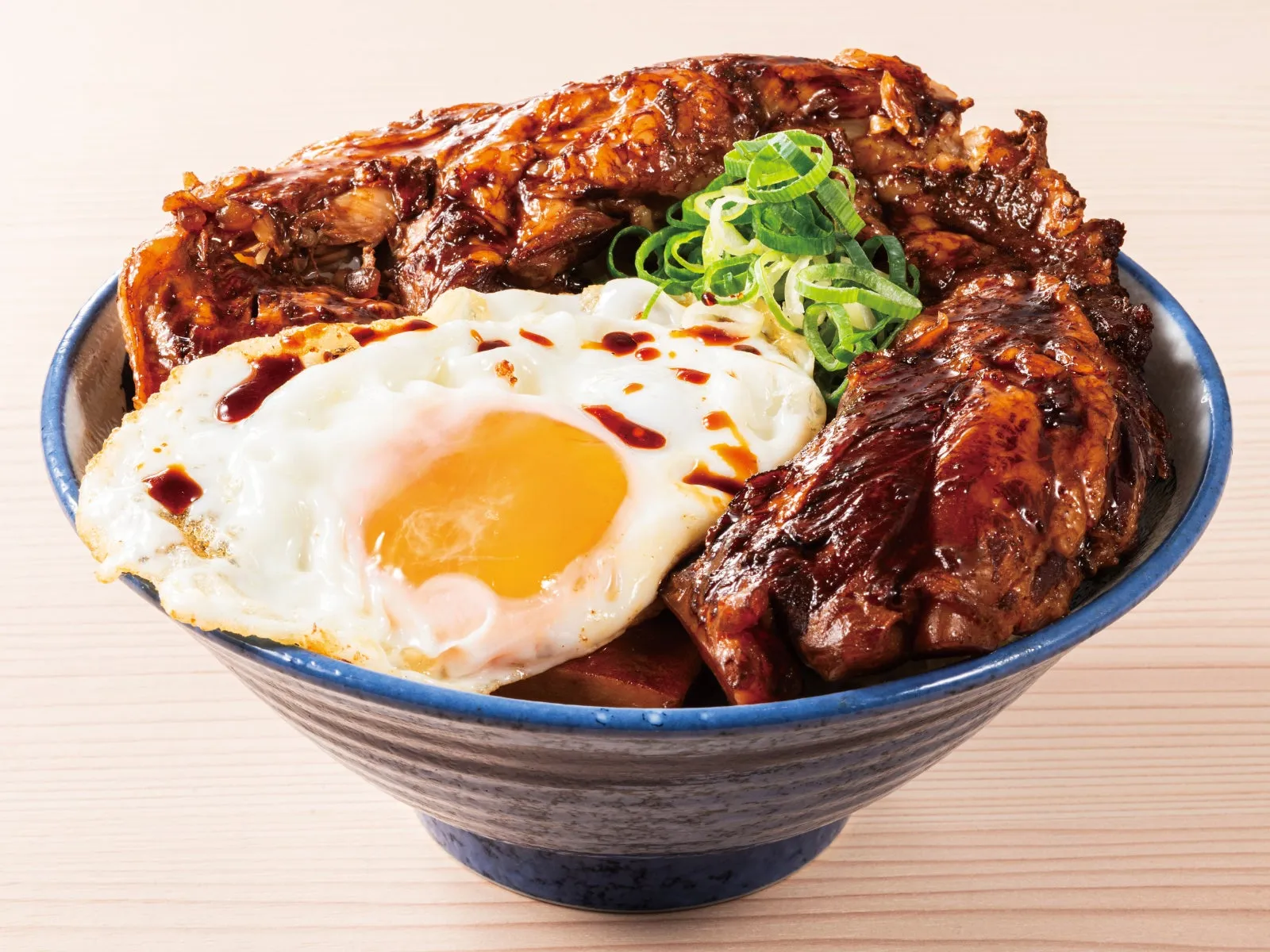 丼に盛られた料理の写真。大きな肉、目玉焼き、ネギが添えられている。