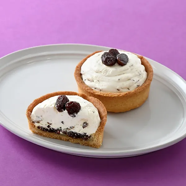 白いクリームが乗ったタルトが2つ、白い皿に乗っている写真です。タルトの上にはレーズンが乗っています。背景は紫です。
