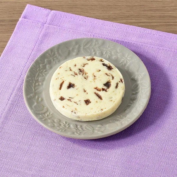 紫色のナプキンに置かれた、飾り模様のある小さな灰色の皿の上に、チョコレートチップのようなものが入ったバターの丸い塊が置かれています。