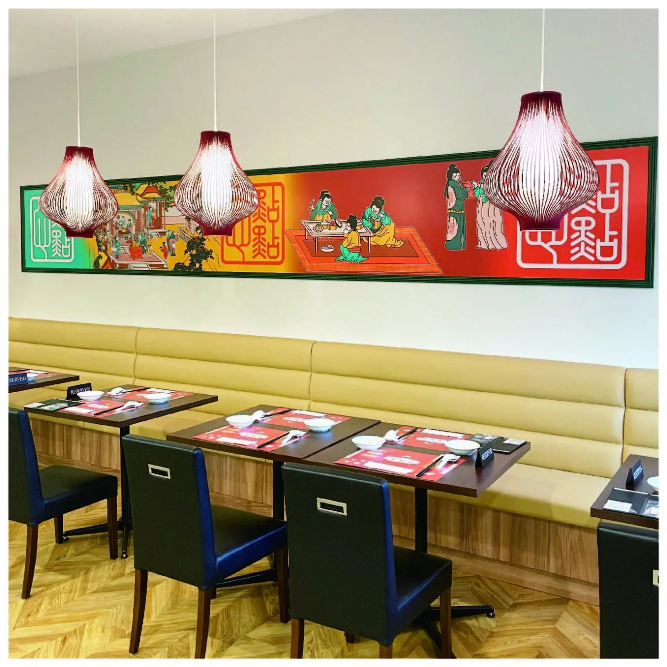 レストランのインテリア。テーブルと椅子があり、壁には絵が飾られ、天井からは照明が吊り下げられています。