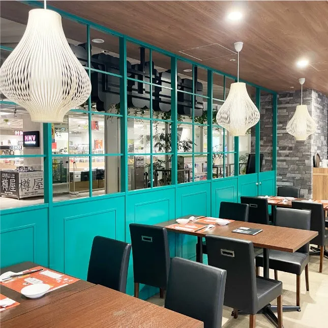 店内には、白くユニークな形のペンダントライトが吊り下げられ、木製のテーブルと黒い革張りの椅子が配置されたモダンな内装のレストラン。窓からは外の景色が見え、明るく開放的な雰囲気を作り出している。