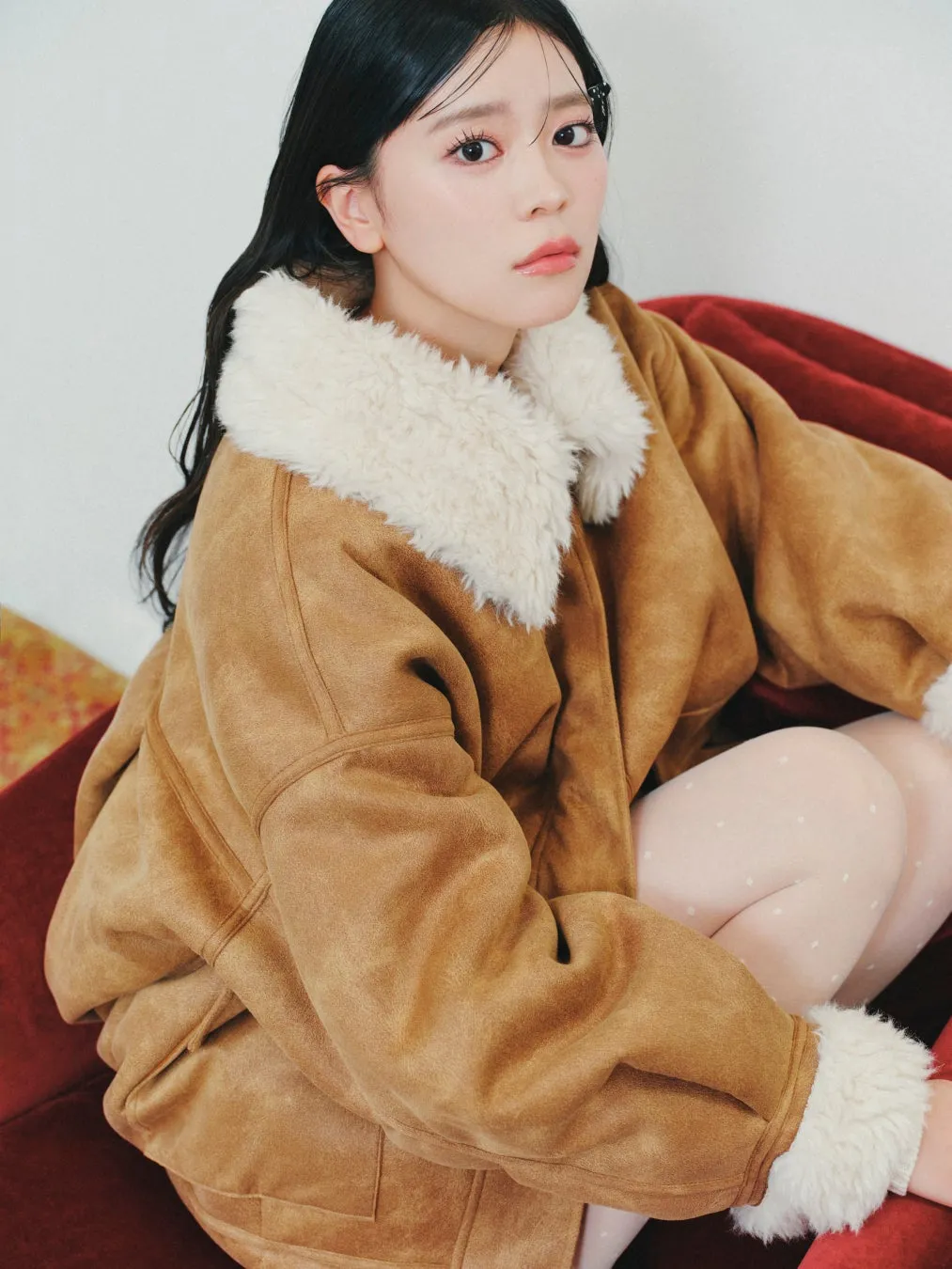 茶色のジャケットを着た女性が赤いソファに座っている写真です。