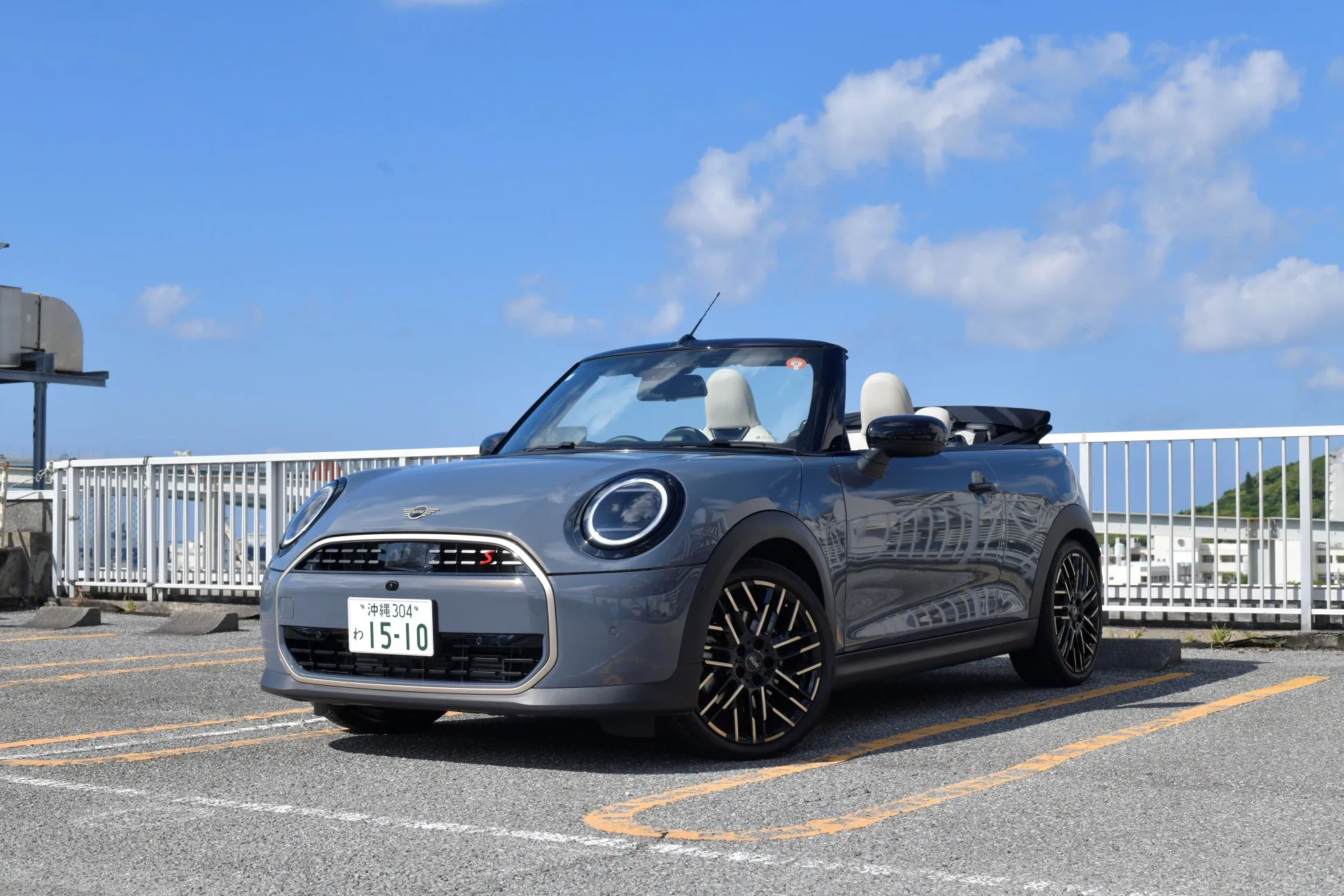 青空の下、駐車場に停まっているグレーのミニコンバーチブルの写真です。