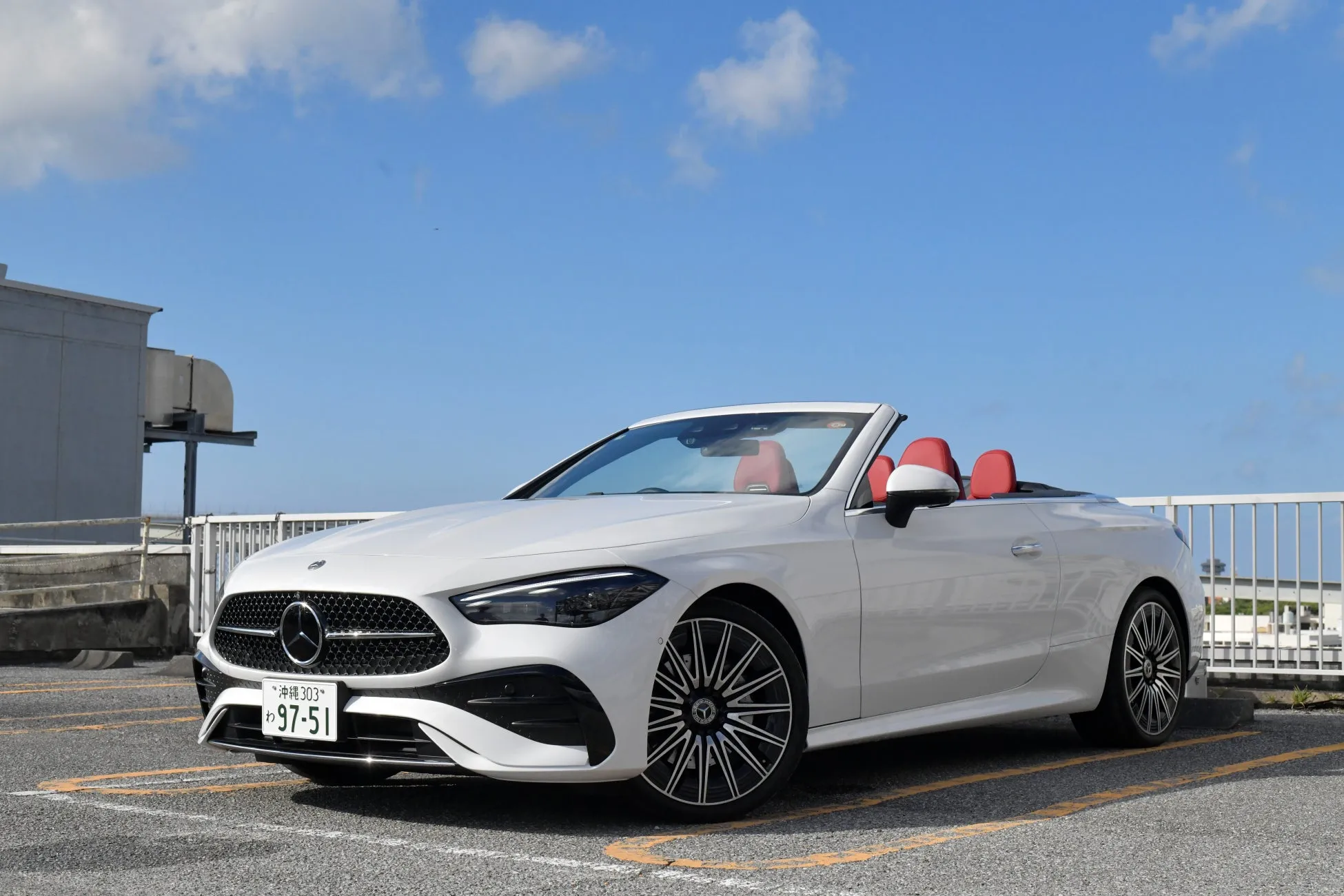 白いメルセデスベンツのオープンカーが駐車場に停まっている写真です。青空と白い雲が背景に広がっています。