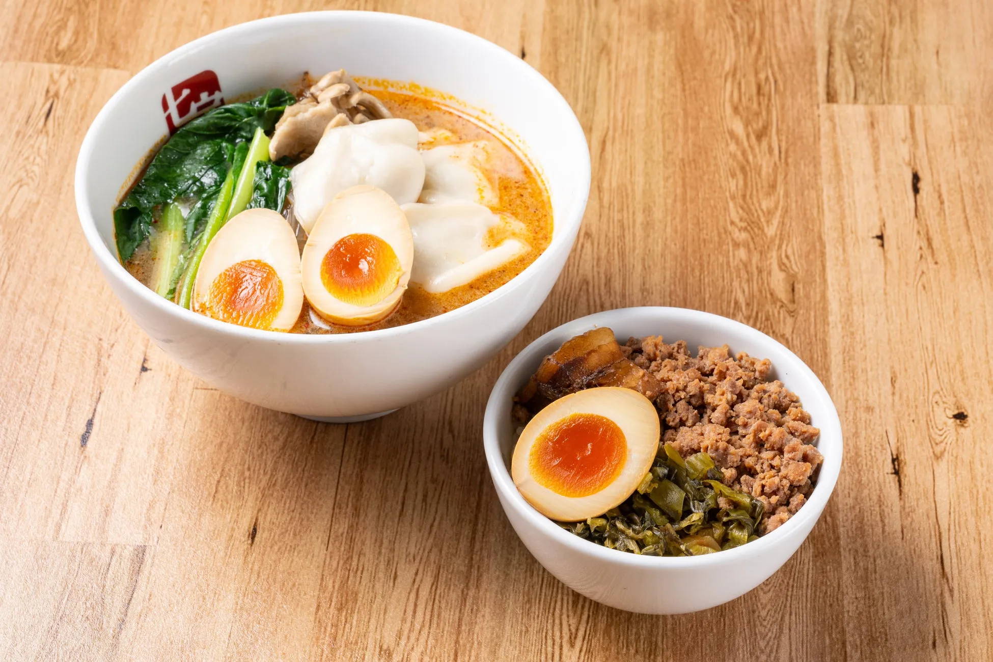 2種類の料理が写った写真。大きな白い器に入った麺料理と、小さな白い器に入ったご飯料理が写っています。どちらの料理にも半熟卵が添えられています。