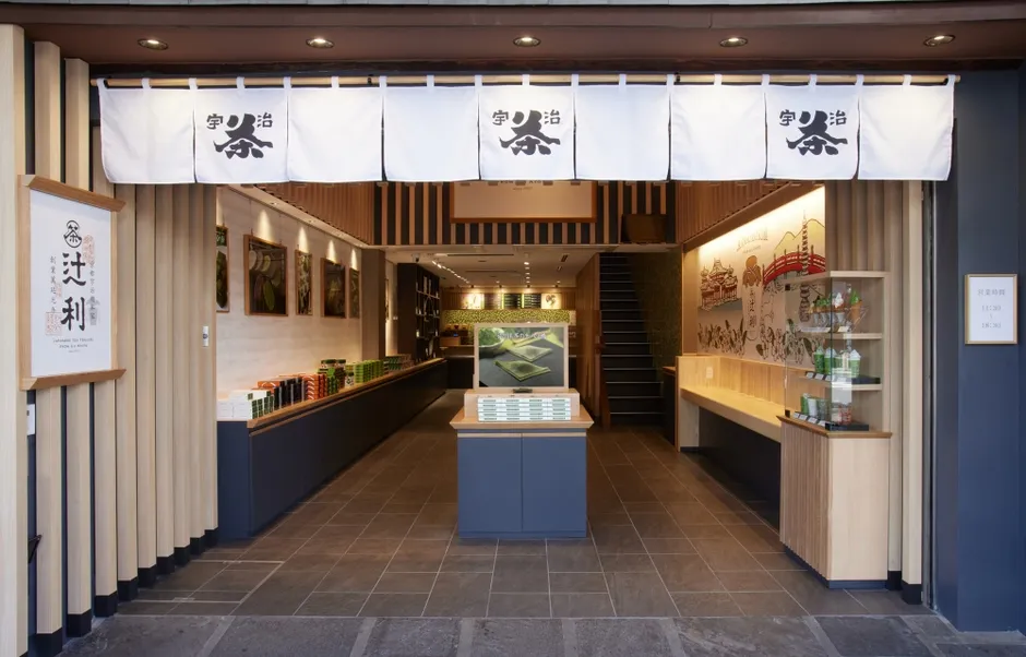 宇治茶の辻利の店舗の正面玄関。白いのれんには「宇治」の文字とマークが描かれ、店内のディスプレイや商品が見える。