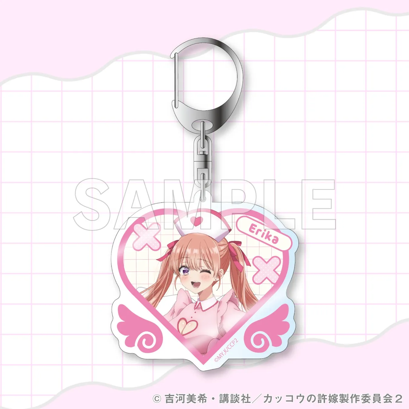ピンク色のハート型のキーホルダー。キーホルダーには、ピンク色の髪の毛の女性のイラストが描かれており、「Erika」の文字が入っている。背景には格子模様がある。
