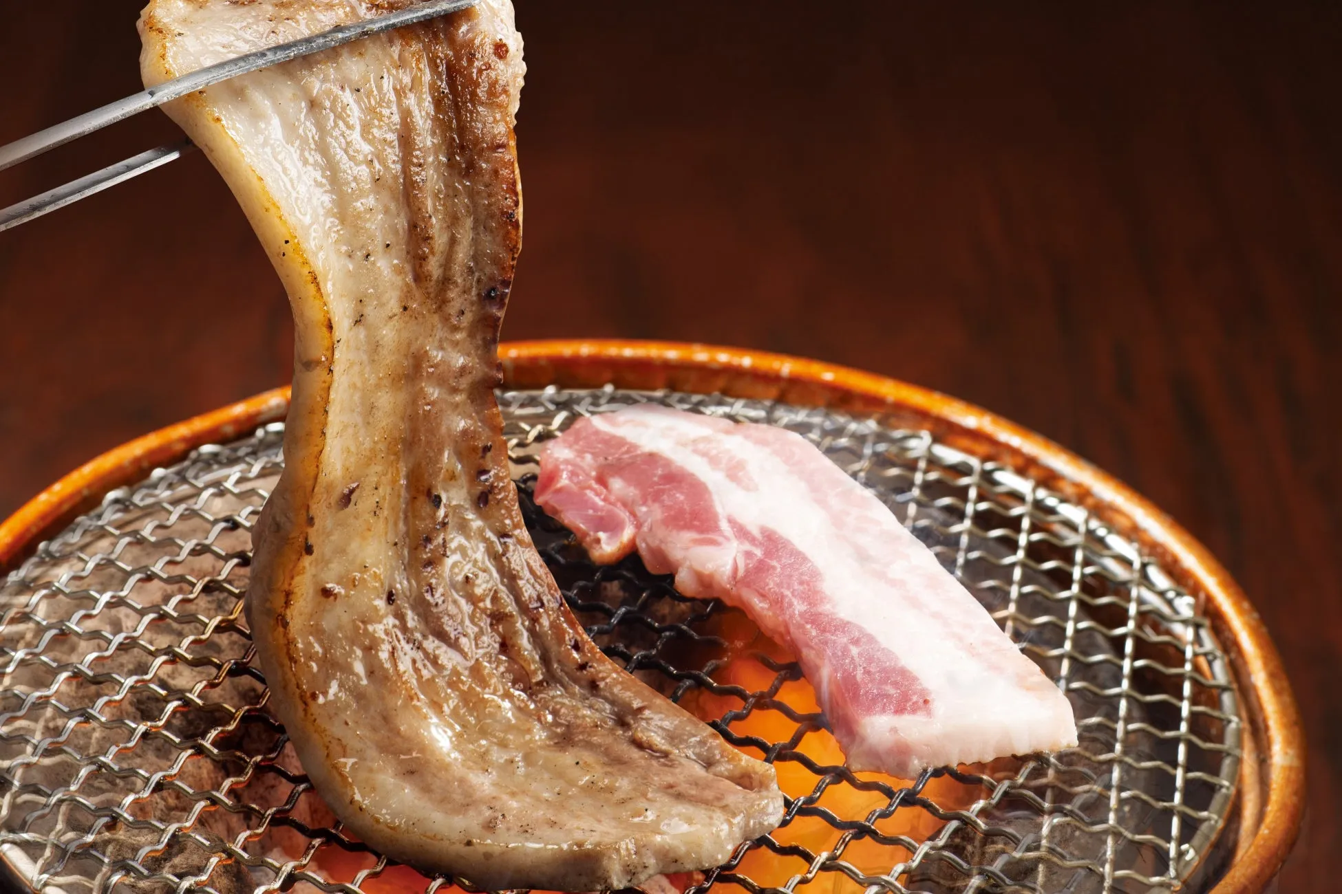 焼き肉をしている様子。焼かれた豚バラ肉と、焼く前の豚バラ肉が写っている。