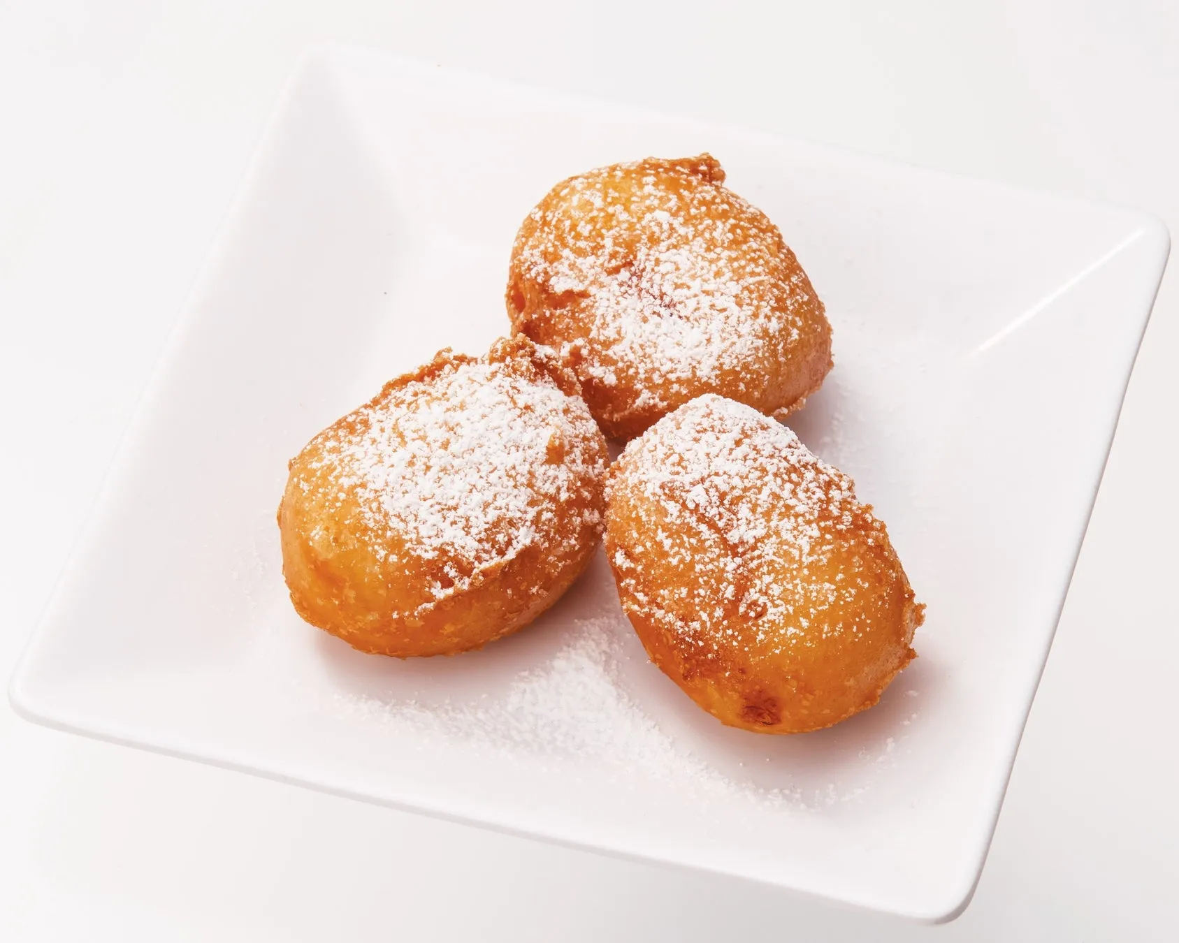 白い皿に3つの揚げドーナツが乗っている画像です。ドーナツには粉砂糖がまぶされています。