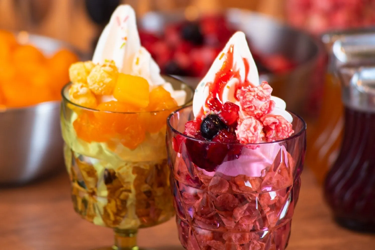 2つのデザートグラスに盛られたソフトクリーム。手前には赤いベリーとポップコーンがトッピングされたもの、奥にはオレンジの果肉とポップコーンがトッピングされたものがある。
