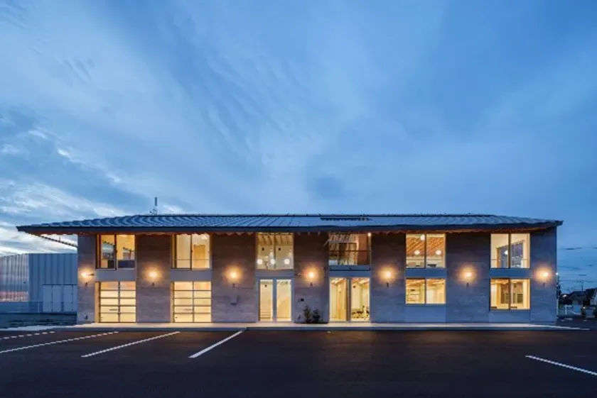 モダンなデザインの建物。駐車場があり、夜空の下でライトアップされている。