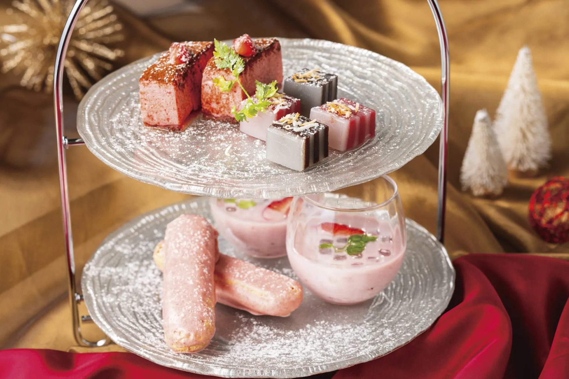 2段のガラスのトレイに、様々なデザートが盛り付けられた写真。上段には、ピンク色のケーキ、四角いゼリー、下段にはピンクのエクレアとデザートが入ったグラスが配置されている。