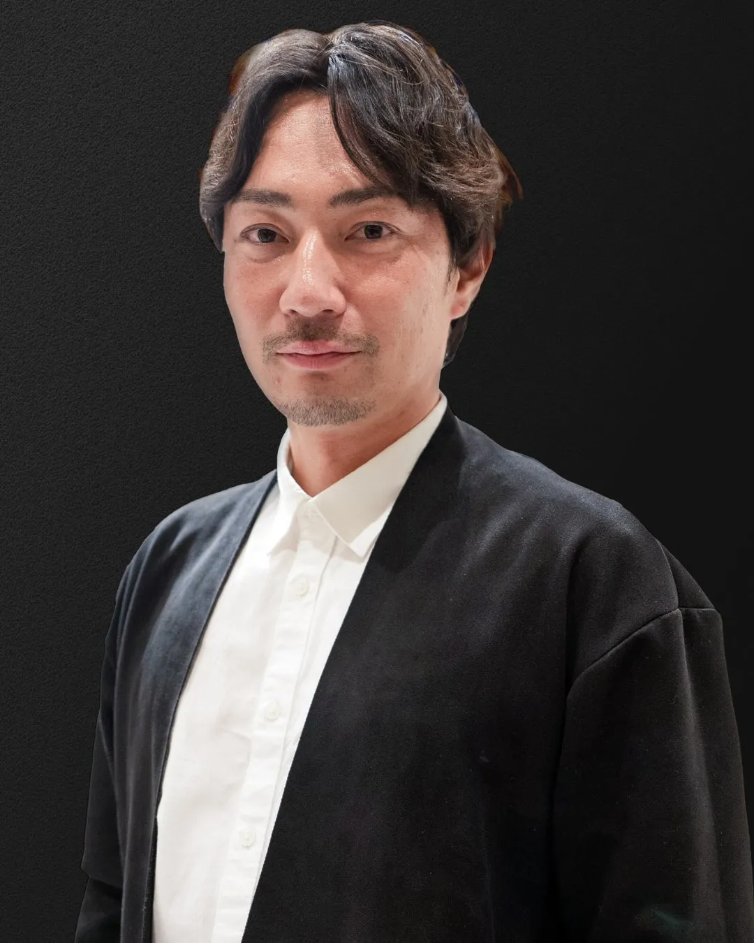 黒い背景に、白いシャツと黒いジャケットを着た男性のポートレート。