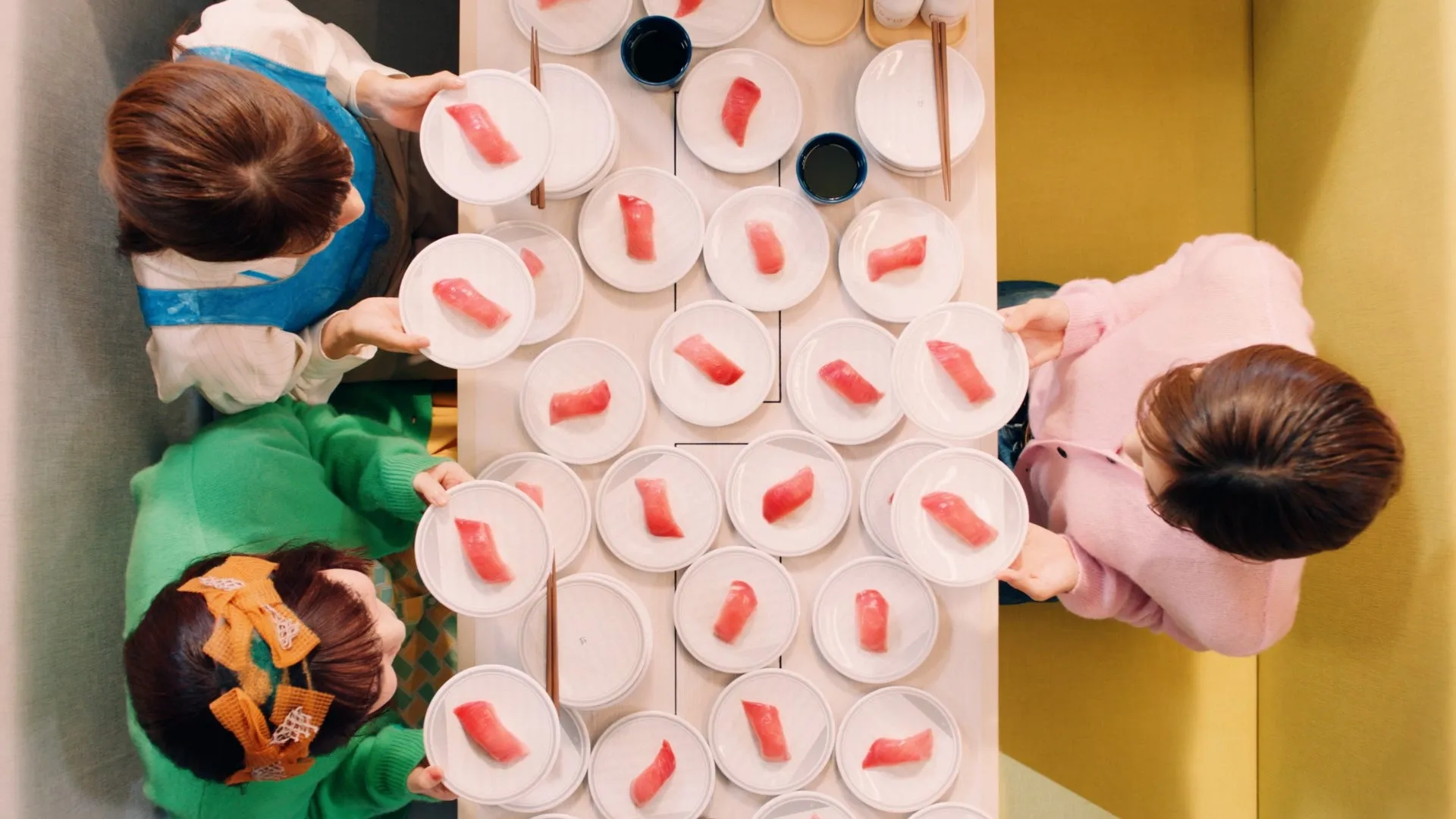 テーブルを囲んで食事をする3人の女性の俯瞰写真。テーブルにはマグロの握りがたくさん並んでいる。