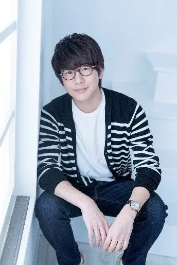 眼鏡をかけた男性が階段に座ってポーズをとっている写真です。