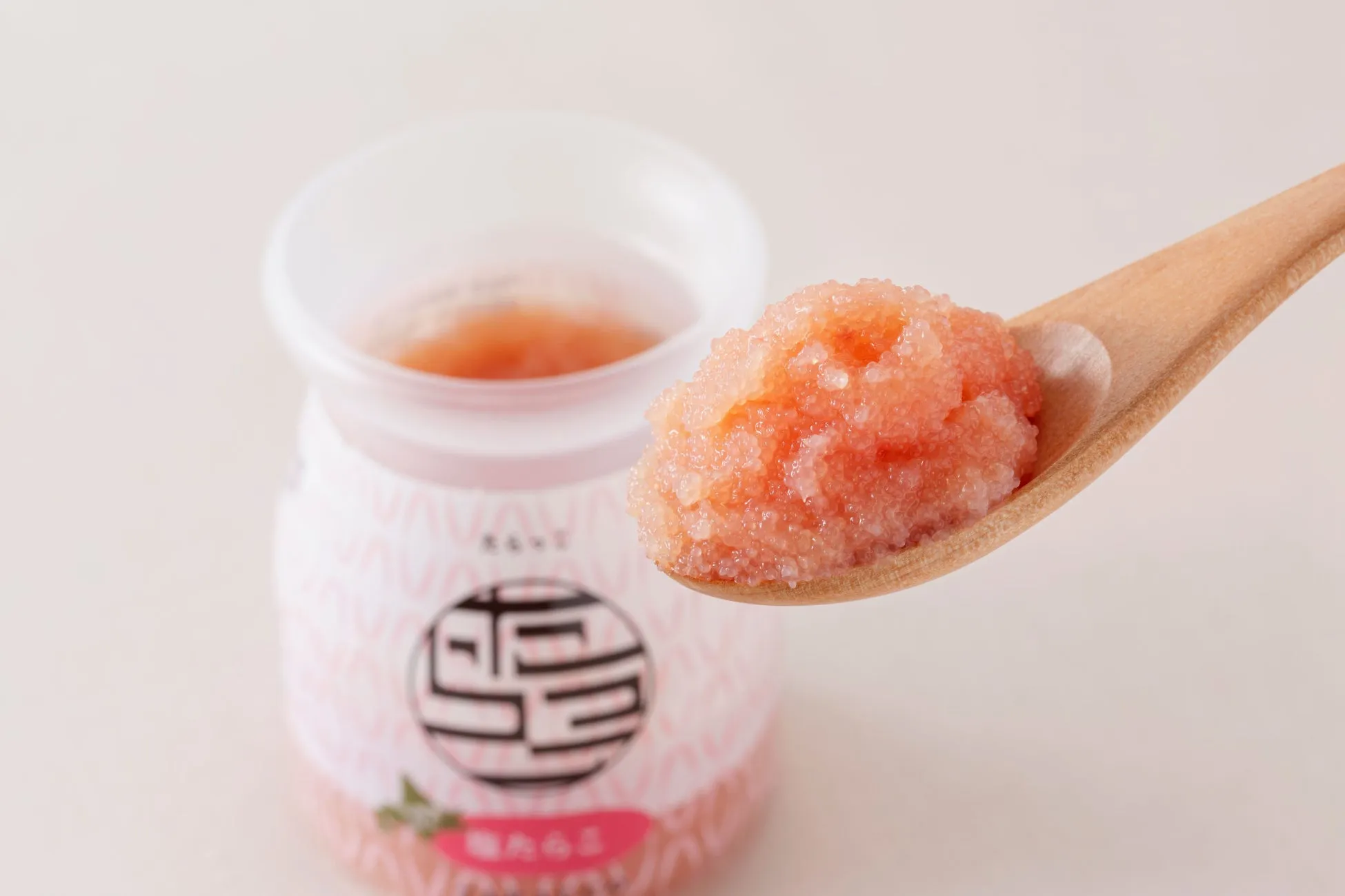 木のスプーンに乗った明太子のクローズアップ。瓶詰めされた明太子が背景にあり、ラベルに日本語の文字が書かれています。