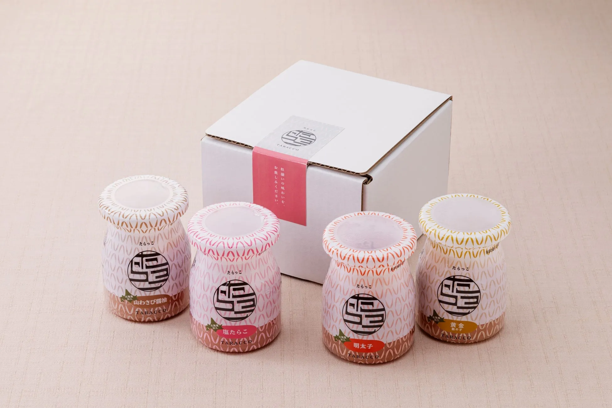 4つの瓶が入った箱の写真。瓶には様々なフレーバーのたらこが詰められており、それぞれ異なる色とデザインのラベルが貼られています。箱には「TARACCO」のロゴと「粒揃い」と書かれた赤い帯があります。