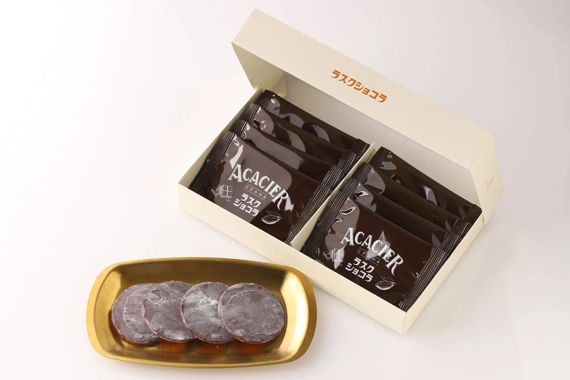 チョコレートのお菓子が箱に入っている写真。箱の中には個包装されたチョコレートラスクが入っており、手前には金色の皿に盛られたチョコレートラスクが写っています。
