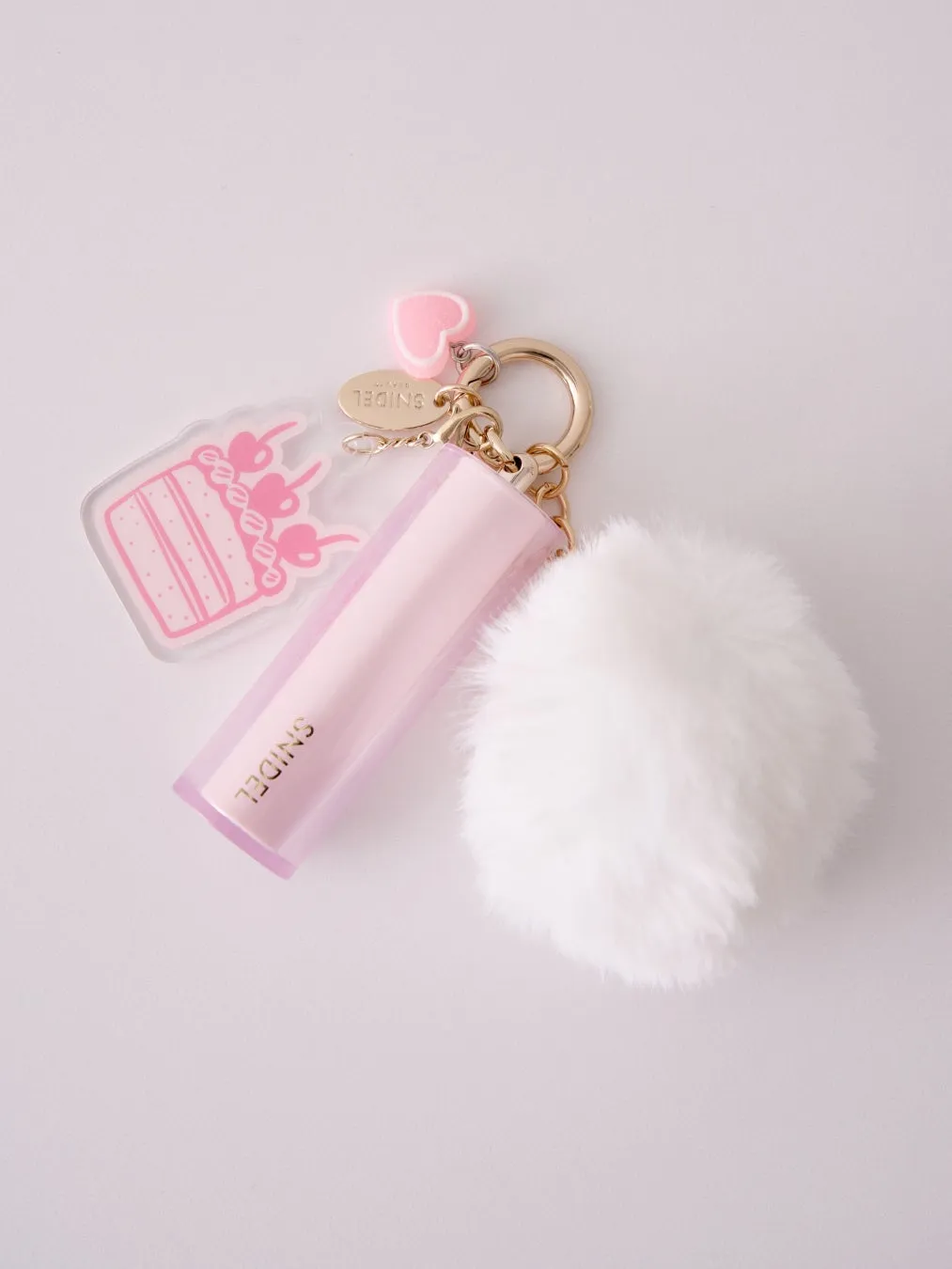 ピンク色のキーホルダー。ケーキのチャーム、ハートのチャーム、白いファーボール、そしてブランド名「SNIDEL」が入ったアイテムが写っています。