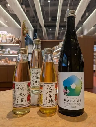 テーブルの上に並んだ、日本のサイダーと日本酒の瓶の集合写真。ラベルには様々な日本語の文字が書かれており、それぞれの商品名や産地を示している。