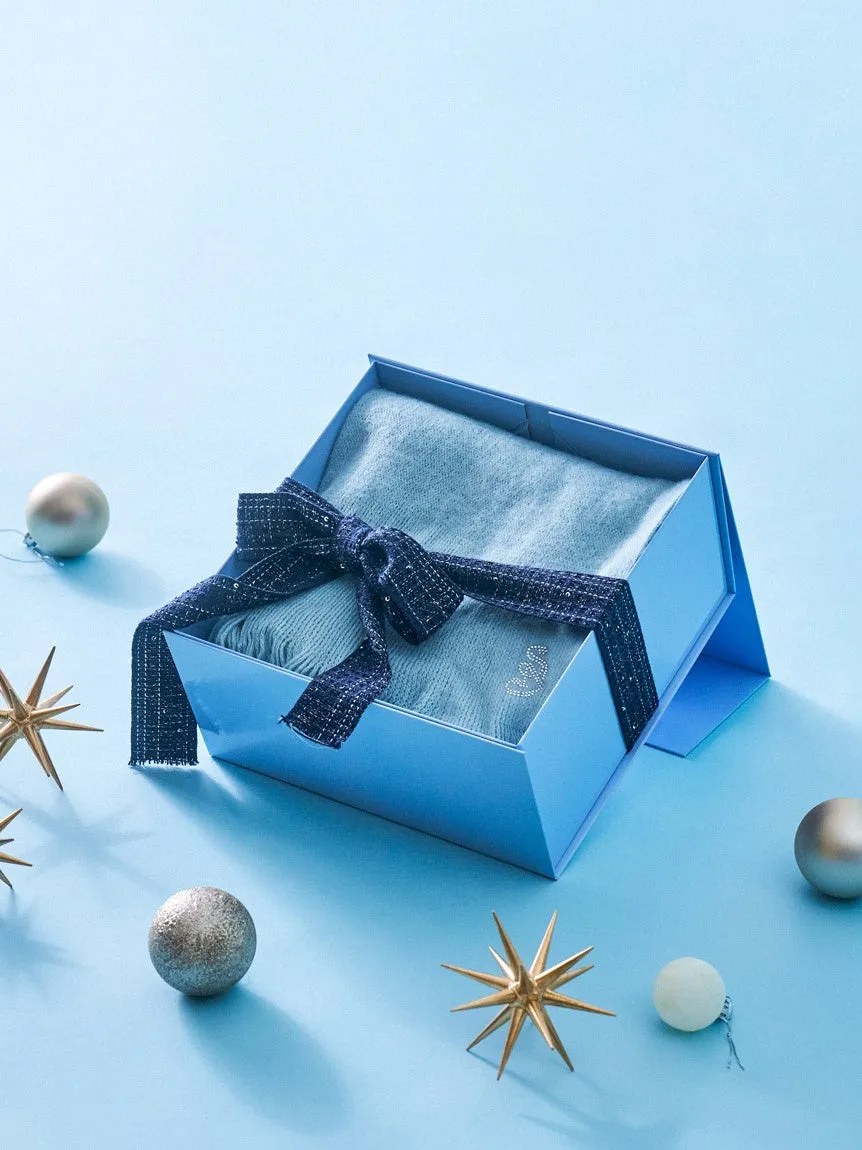 青い箱に入ったギフトセットの写真。箱にはリボンがかけられており、中にはスカーフが入っている。周りにはクリスマスのオーナメントが散りばめられている。