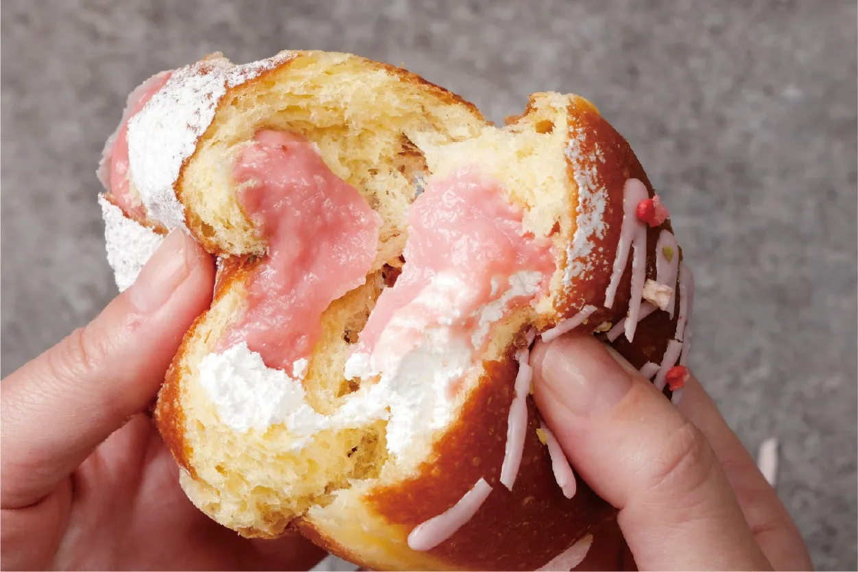 ドーナツが半分に割られており、ピンク色のクリームと白いクリームがたっぷり詰まっている様子が写っています。