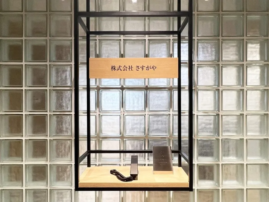 ガラスブロックの壁を背景に、木製の棚に置かれた会社名を表示したディスプレイ。