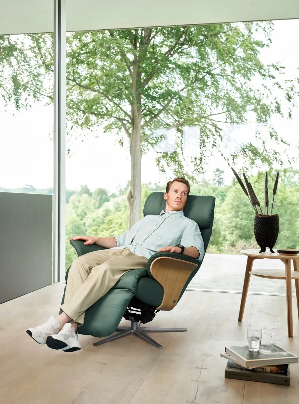 男性が緑色のリクライニングチェアに座り、窓の外の木々を眺めている写真です
