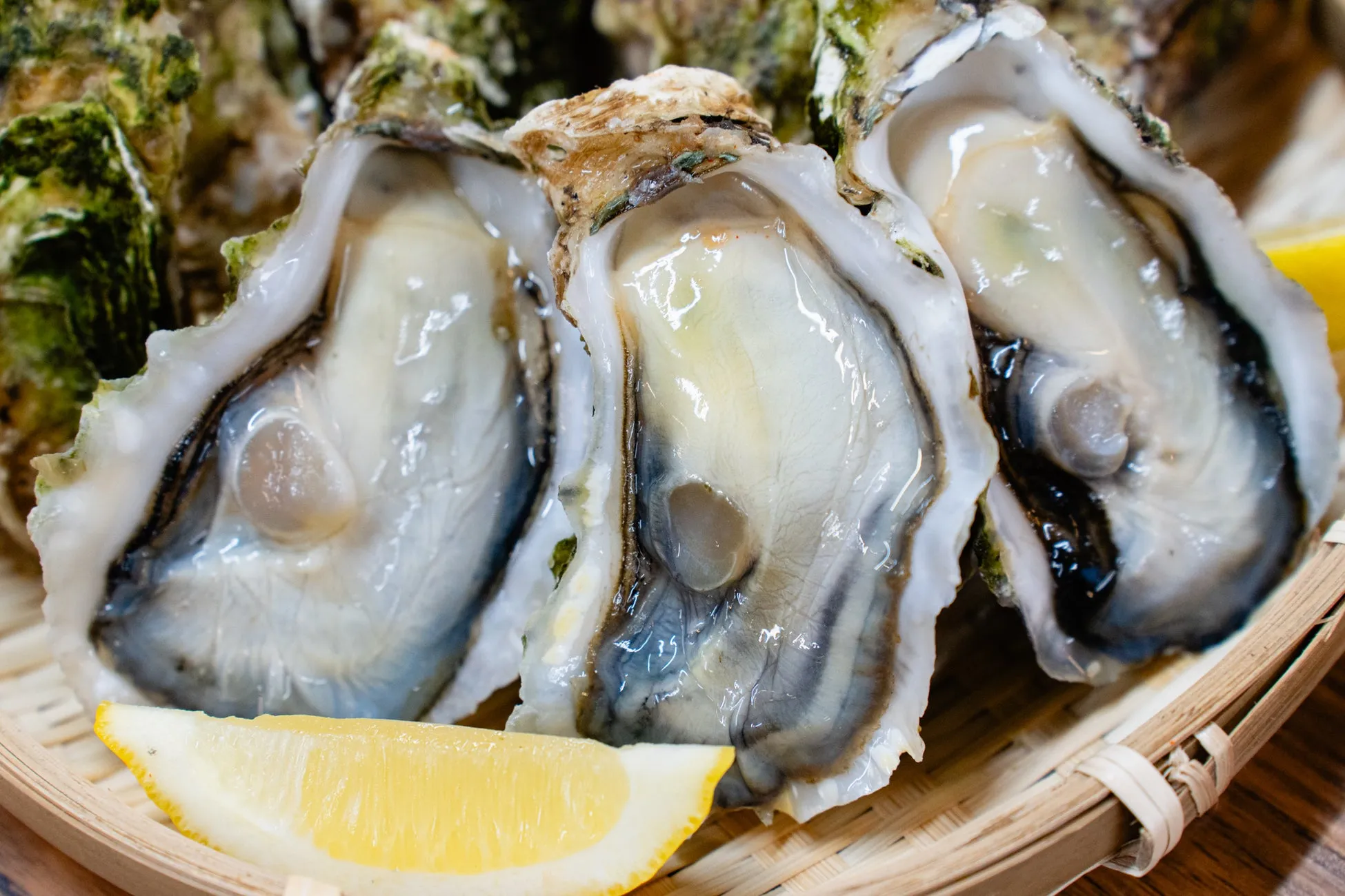 カキのクローズアップ写真。レモンが添えられており、木製の皿の上に置かれている。