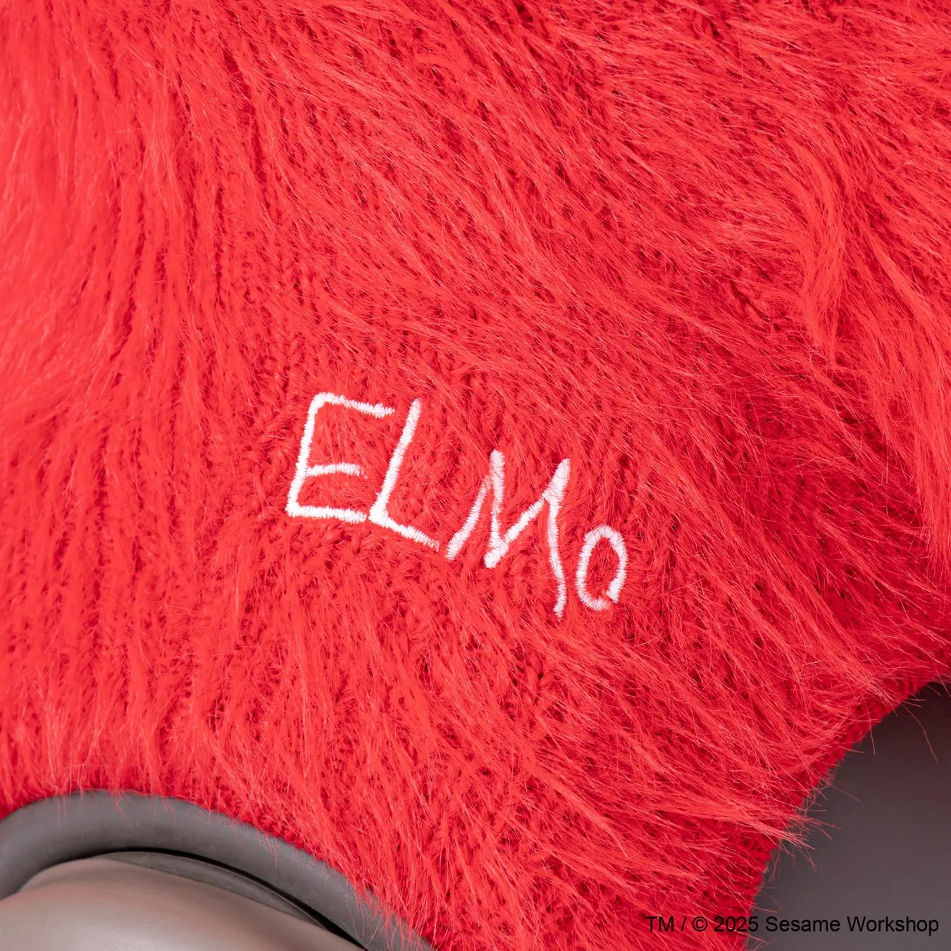赤色のふわふわしたテクスチャに「ELMO」の文字が白く刺繍されています。下部には、著作権情報が表示されています。