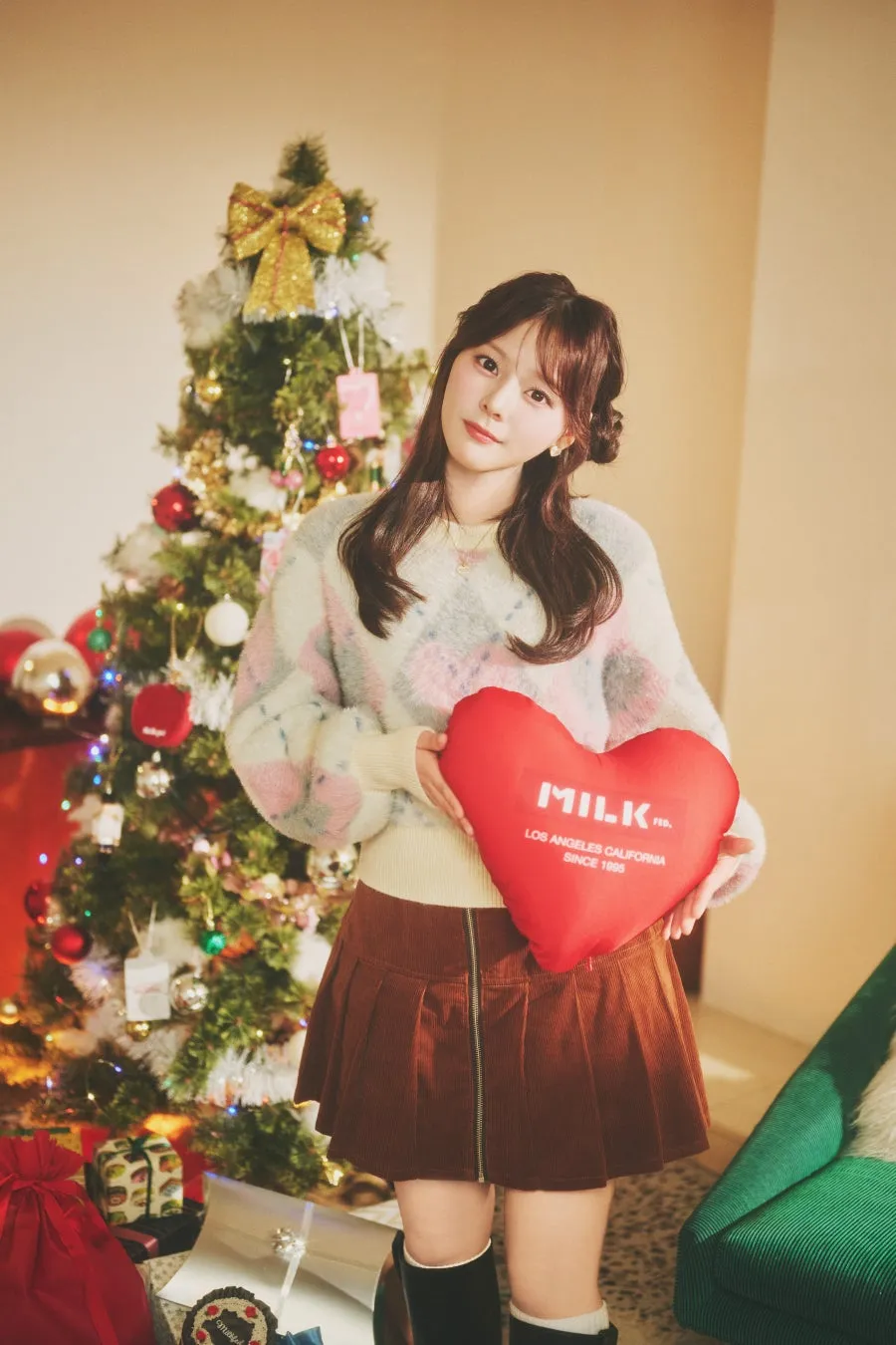 クリスマスツリーの前に立って、赤いハート型のクッションを持っている女性のポートレートの画像