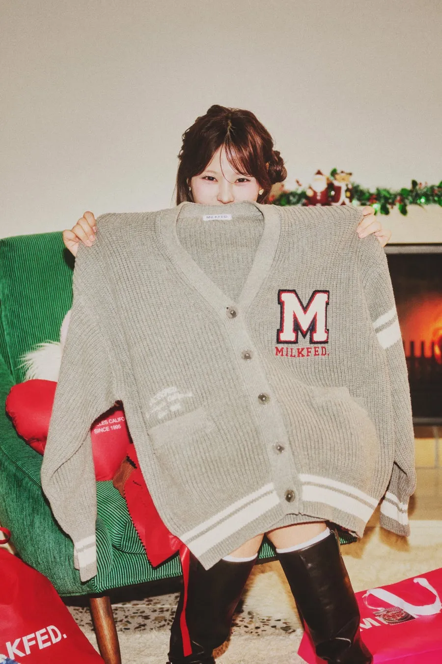 女性が「MILKFED」ロゴのグレーのカーディガンを持ち、顔を隠すようにしている画像