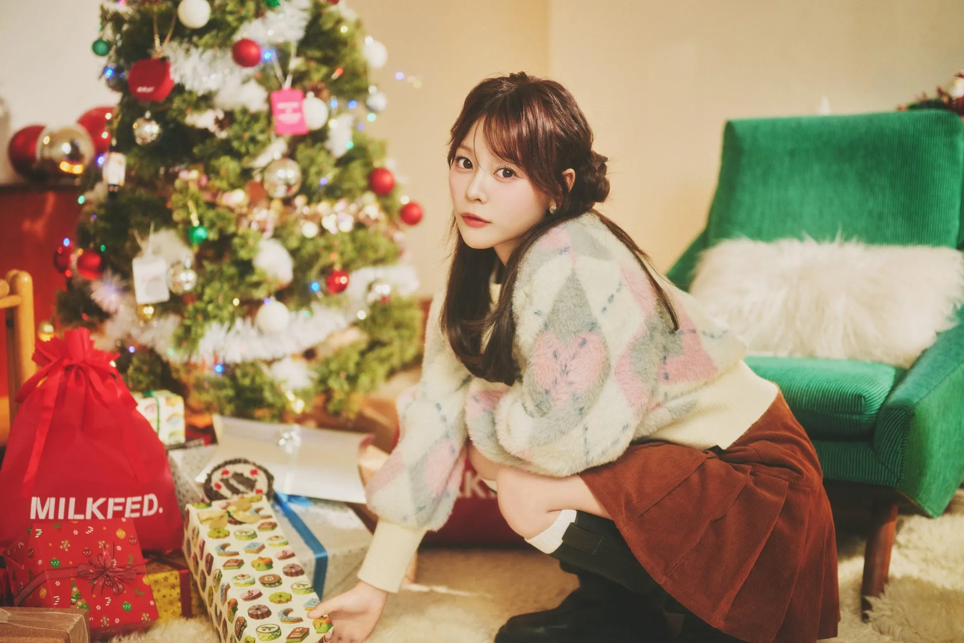 クリスマスツリーの横でプレゼントを開けようとしている女性の画像