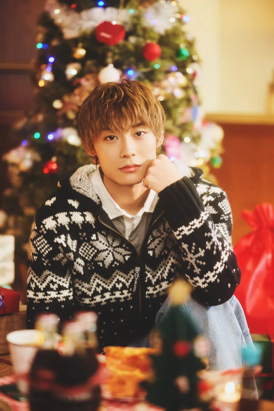 クリスマスツリーを背景に、男性が顎に手を当ててカメラを見つめている画像