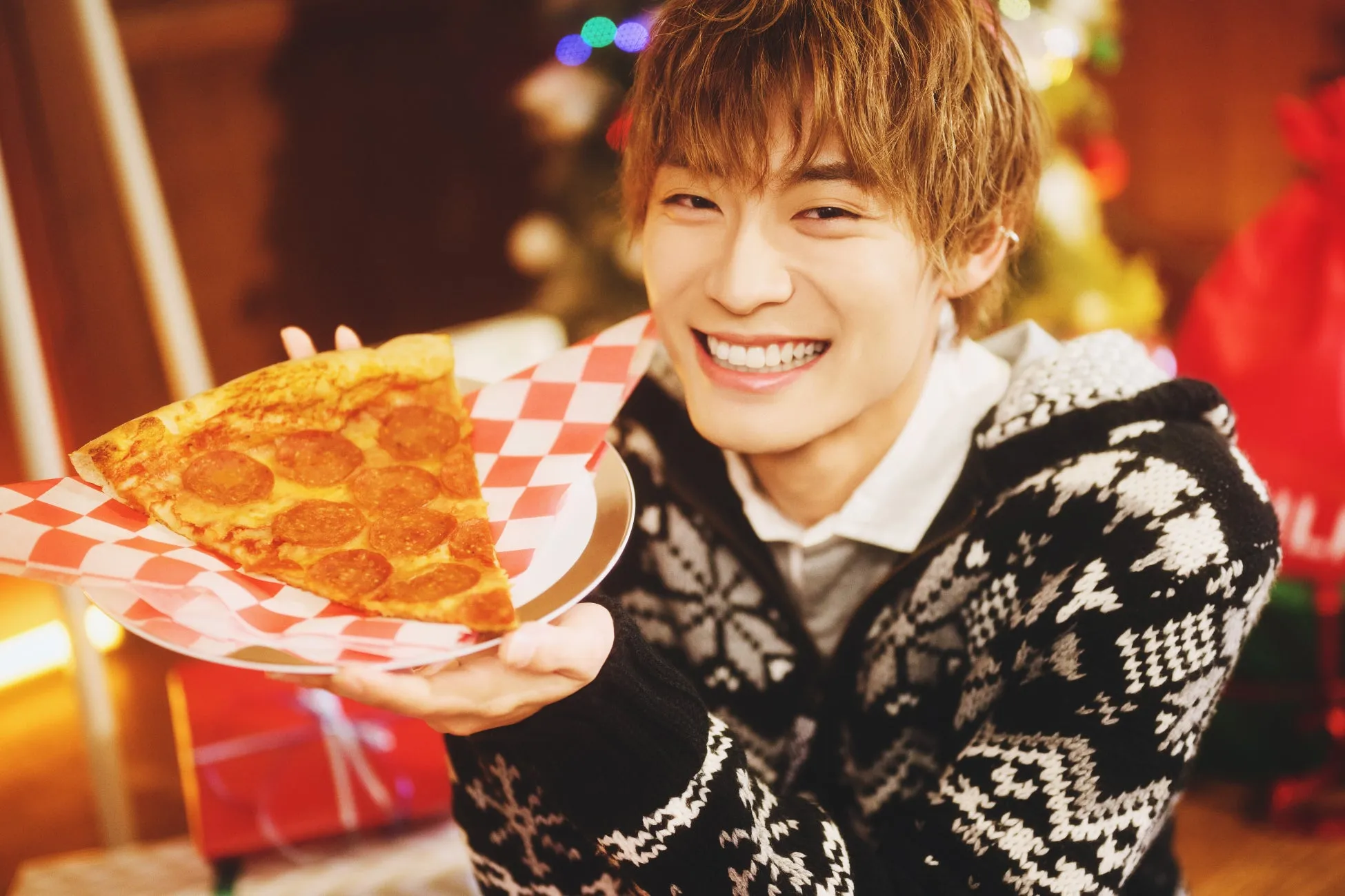 笑顔の男性がピザの1切れを持っています。背景にはプレゼントやクリスマスツリーの飾りの画像