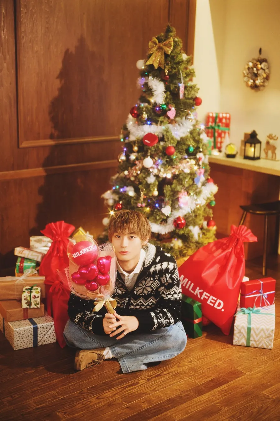 クリスマスツリーの前に座っている男性。赤いハート型の風船、プレゼントの画像