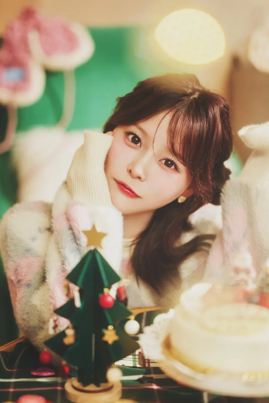 クリスマスをテーマにした女性のポートレート。白いセーター、クリスマスツリー、ケーキと写っている画像