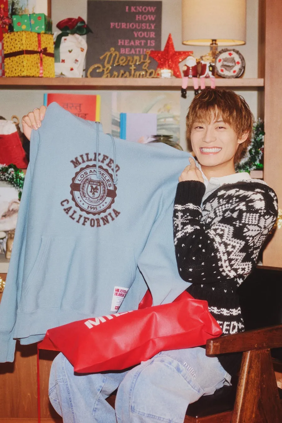 男性が水色のパーカーと赤い袋を持ち、笑顔でカメラを見ている画像