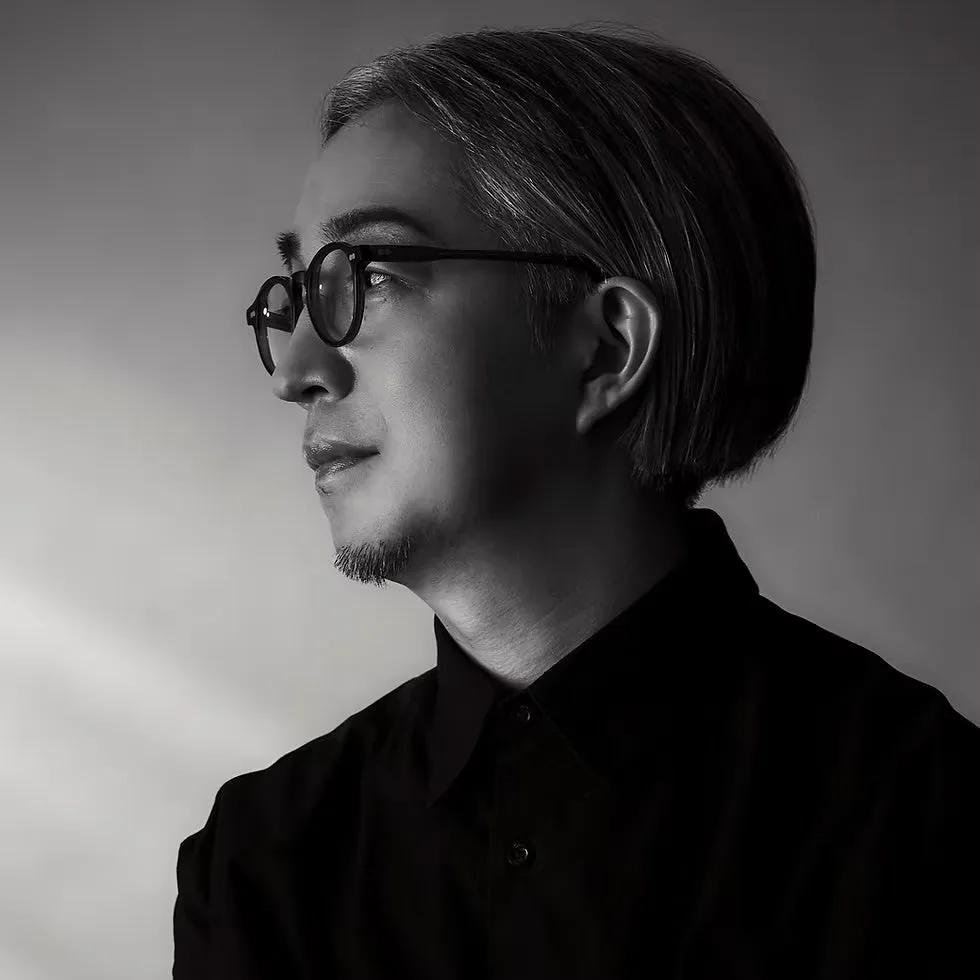 眼鏡をかけた男性のモノクロポートレート。彼は黒いシャツを着ていて、カメラから目をそらしている。